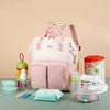 Sac à langer rose entouré d'accessoires de bébé : biberons, lait, lingettes et couches - Bébé Lova