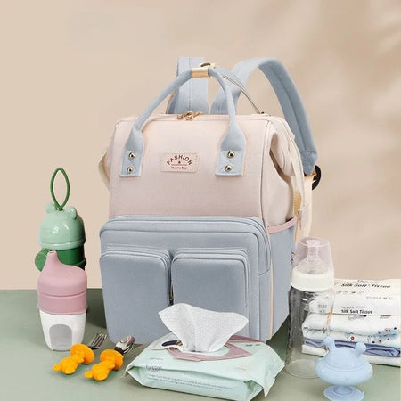 Sac à langer rose et bleu présenté sur une table avec biberons et accessoires de bébé - Bébé Lova