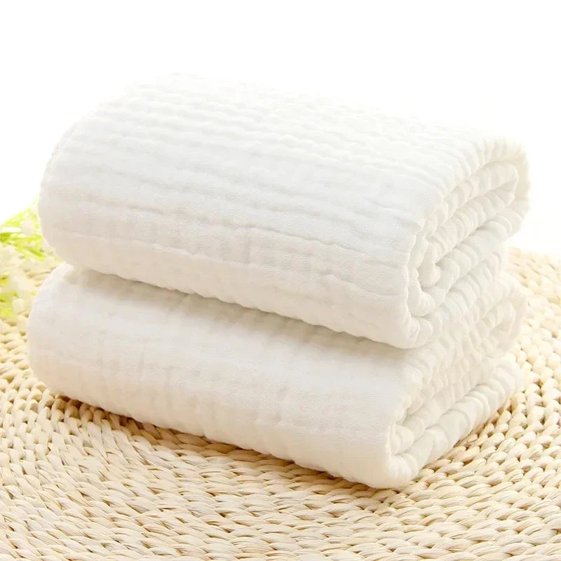 Serviette de bain bébé blanche pliée en mousseline sur tapis tressé - Bébé Lova