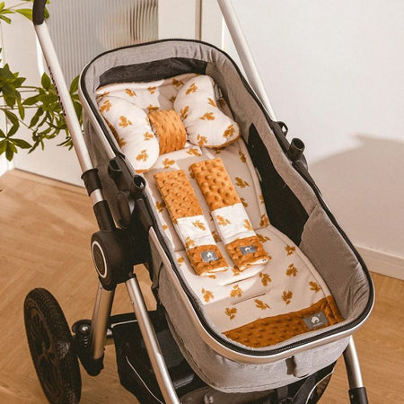Ensemble matelas, coussin et protège-ceintures motif feuilles ocre installé dans une nacelle de poussette vue de dessus - Bébé Lova