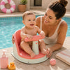 Bébé assis dans un siège de bain portable corail au bord d'une piscine avec sa maman à ses côtés dans un environnement sécurisé et ensoleillé - Bébé Lova