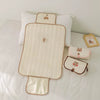 Tapis à langer matelassé déplié avec rabat et deux pochettes pliées présentés sur un lit - Bébé Lova