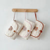 Trois tapis à langer pliés en pochette suspendus à des patères en bois - Bébé Lova