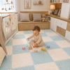 Bébé jouant assis sur un tapis puzzle CozyMat bleu clair et écru dans une chambre de bébé - Bébé Lova