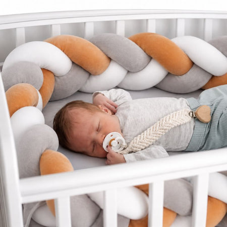Bébé endormi dans un lit à barreaux protégé par un tour de lit tressé gris, caramel et blanc - Bébé Lova