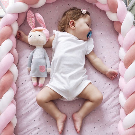 Bébé dormant dans un couffin entouré d’un tour de lit tressé rose poudré et blanc - Bébé Lova