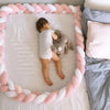 Bébé dormant entouré d’un tour de lit tressé rose et blanc NestBraid dans un espace sécurisé - Bébé Lova