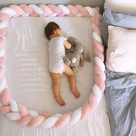 Bébé dormant entouré d’un tour de lit tressé rose et blanc NestBraid dans un espace sécurisé - Bébé Lova
