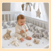 Bébé assis entouré d'une tresse de lit gris et blanc avec peluches - Bébé Lova