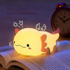 Veilleuse axolotl allumée en lumière chaude posée sur un livre avec illustrations d'ailes et d'étoiles - Bébé Lova