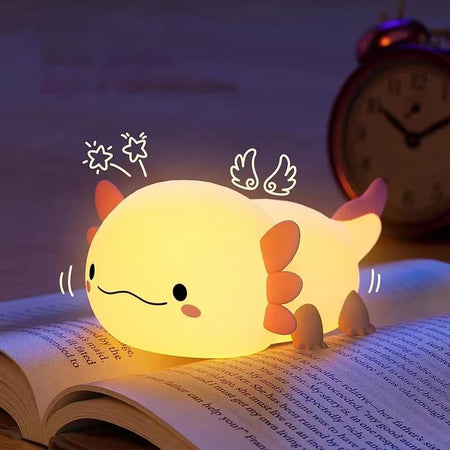 Veilleuse axolotl allumée en lumière chaude posée sur un livre avec illustrations d'ailes et d'étoiles - Bébé Lova
