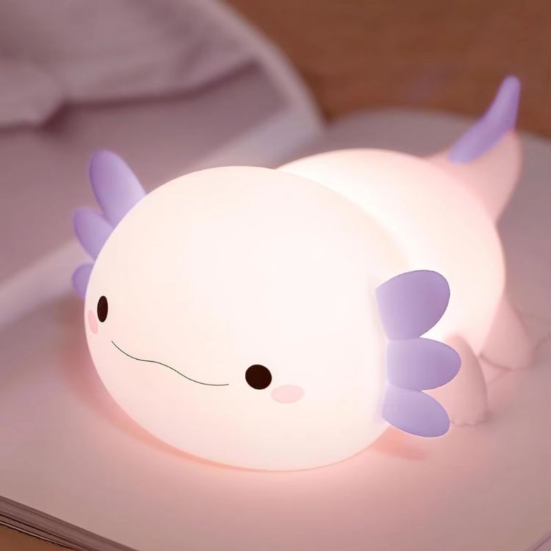 Veilleuse axolotl en silicone allumée à nageoires violettes posée sur un livre - Bébé Lova