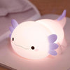 Veilleuse axolotl en silicone allumée à nageoires violettes posée sur un livre - Bébé Lova