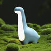 Veilleuse bébé en forme de dinosaure bleue allumée posée sur de la mousse végétale - Bébé Lova