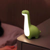 Veilleuse dinosaure verte allumée sur une table de chevet dans une chambre - Bébé Lova