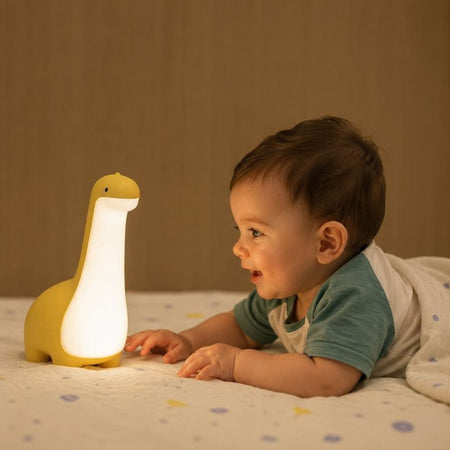 Bébé allongé sur un lit observant la veilleuse dinosaure jaune allumée - Bébé Lova
