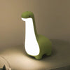 Veilleuse dinosaure verte allumée posée sur un canapé - Bébé Lova