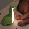 Veilleuse dinosaure verte allumée à côté d'un bébé endormi - Bébé Lova